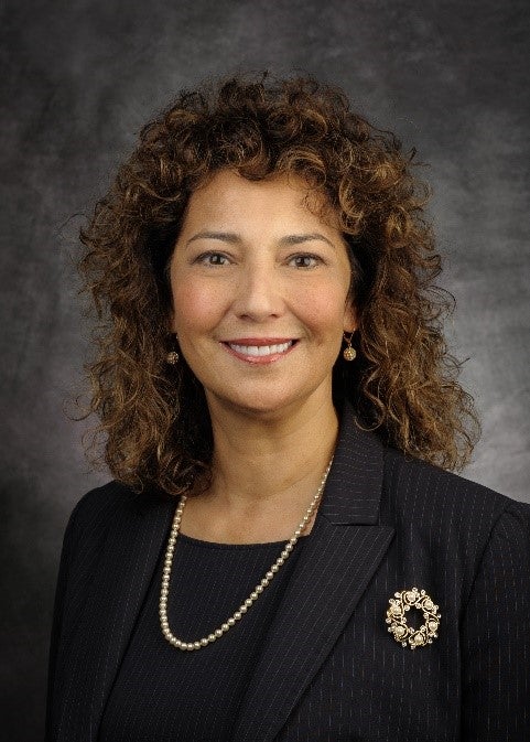 Latina woman in blazer with curly hair, smiling