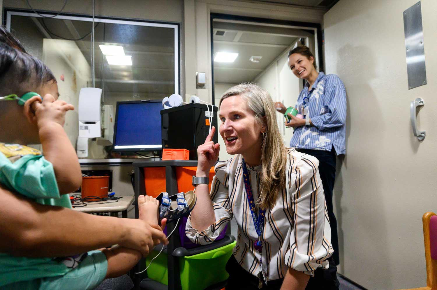 A doctor uses sign language to communicate with a toddler while a parent looks on
