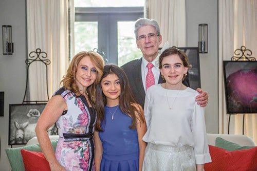 Woman in floral dress next to two pre-teen daughters, Dr. Frenk standing behind, in the Frenk family living room