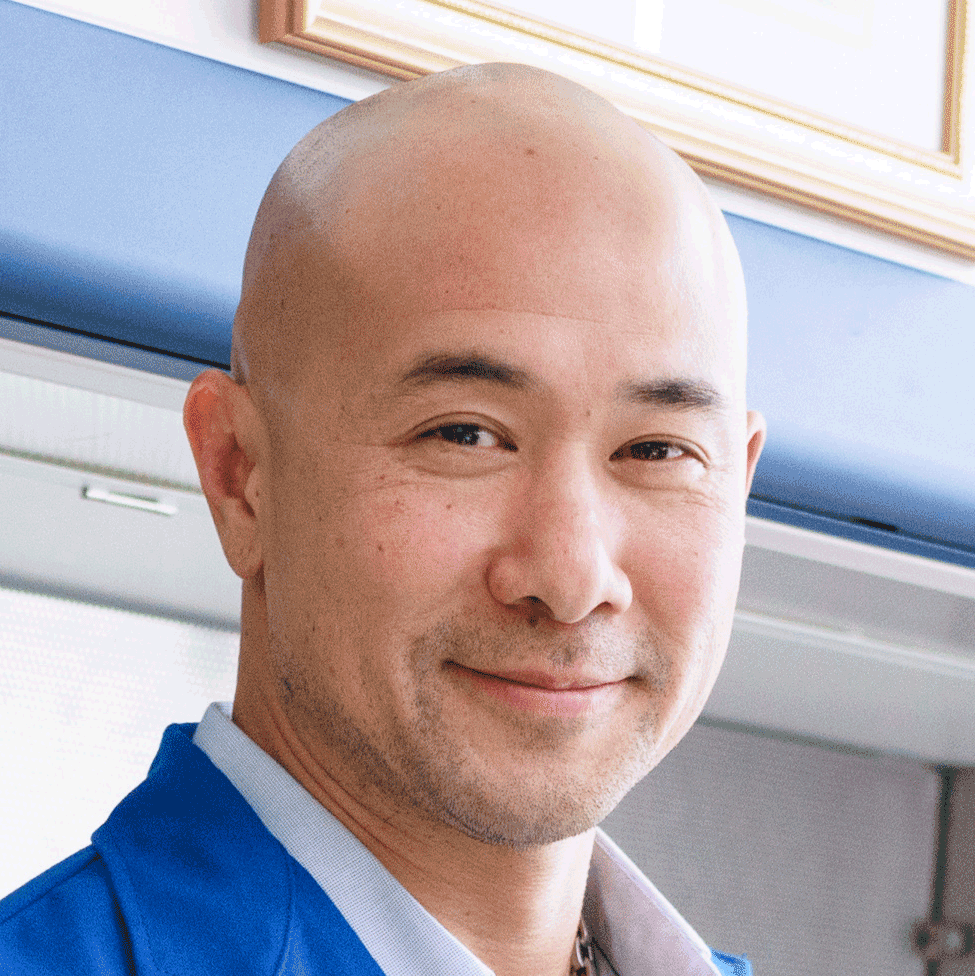 Man with shaved head in blue coat smiles at camera