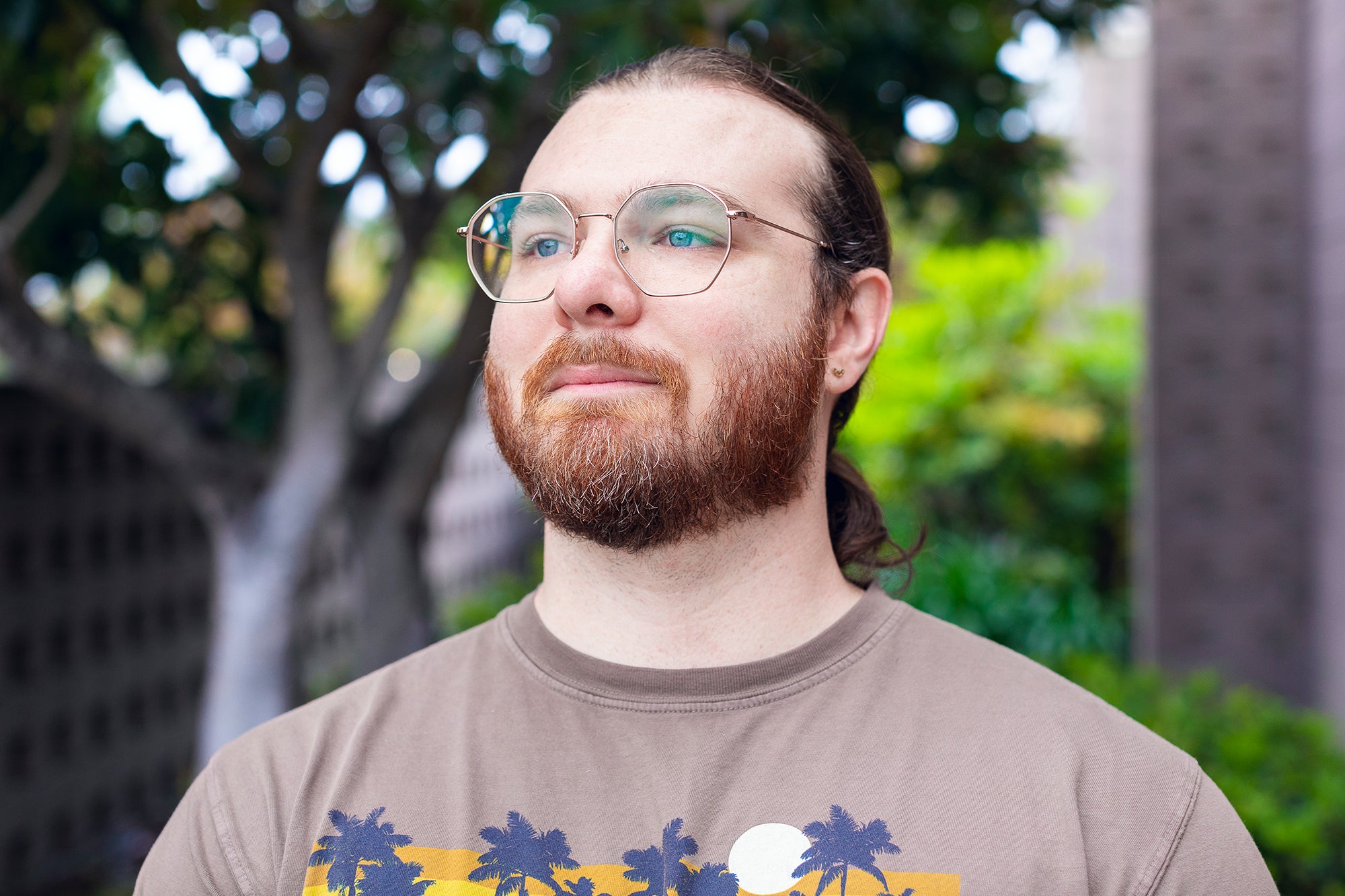 Student with glasses, a beard, and hair pulled back into a ponytail looks off-camera