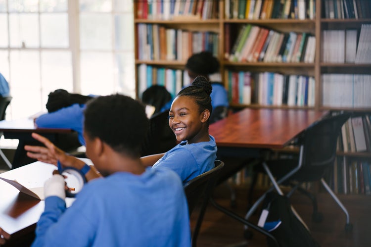 A teenage girl looks over her shoulder and smiles at a classmate in a classroom