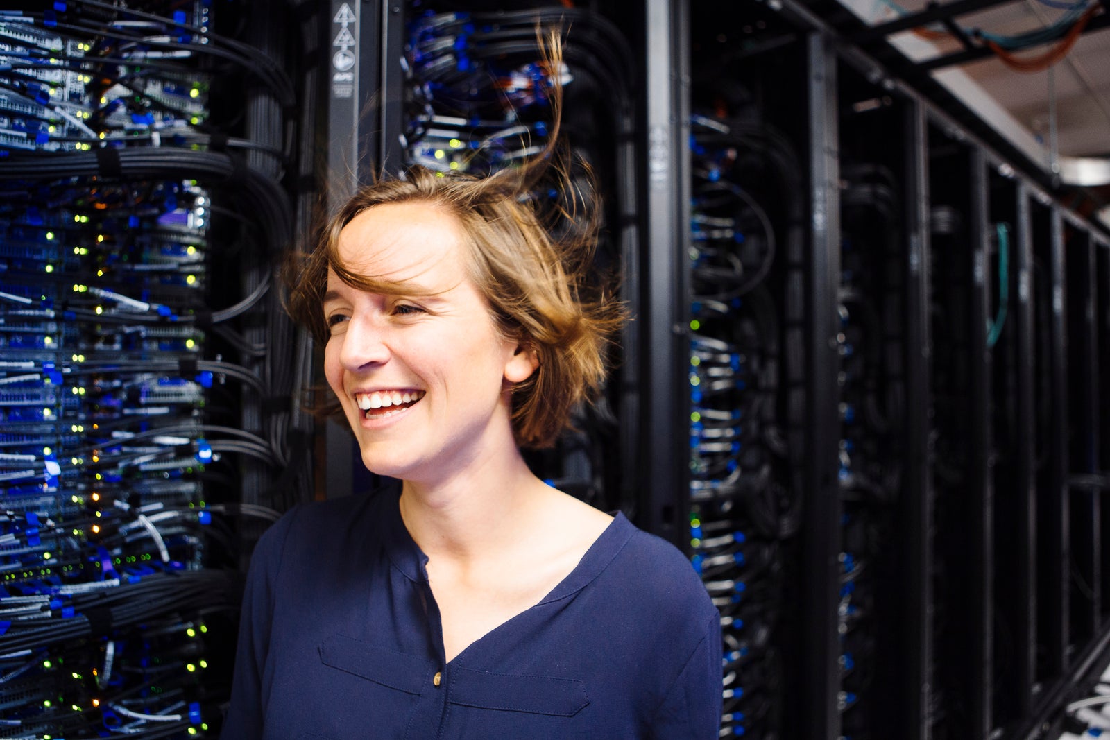 Professor Molly Roberts smiles in half-profile, standing next to a server bank. Breeze from the cooling fans blows her hair askew.