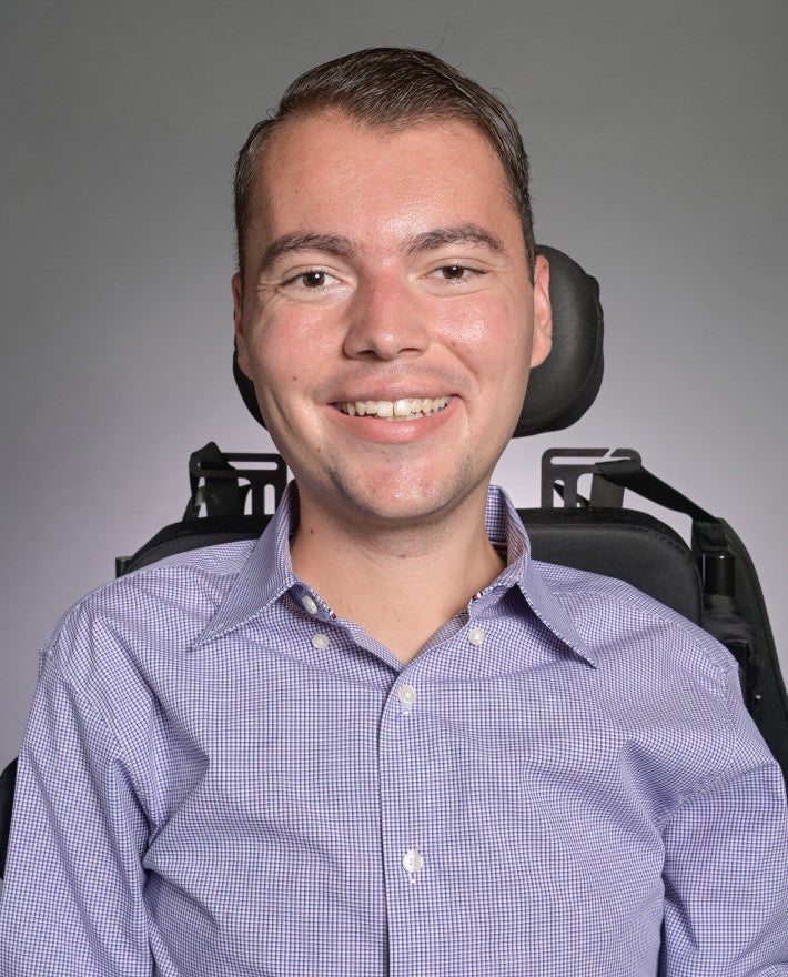 Ryan Manriquez smiles for a professional headshot wearing a blue button-up shirt against a gray backdrop.