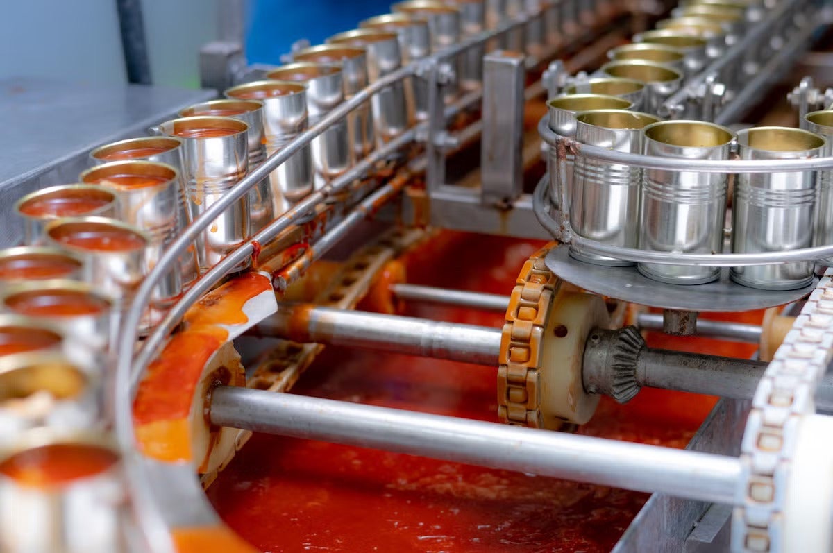 Open cans with red liquid pass on the left side while a conveyer belt with closed cans passes on the right