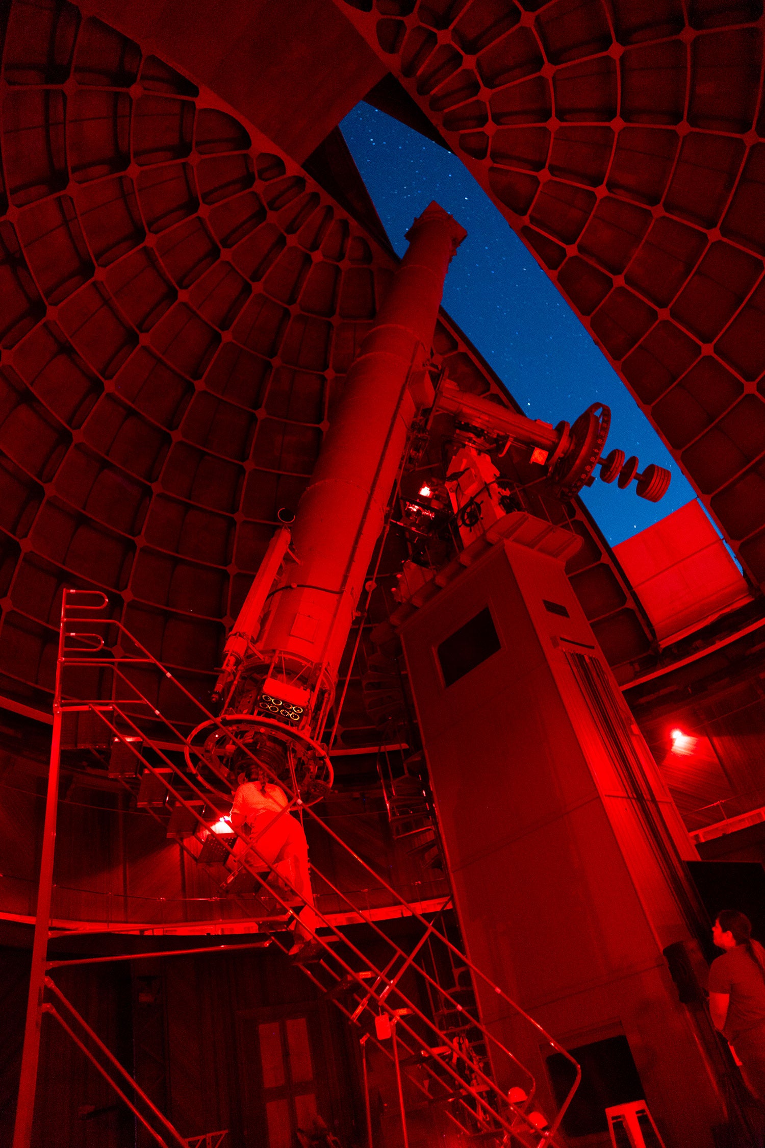 A telescope pointed at the sky through an opening in a dome, lit by red light