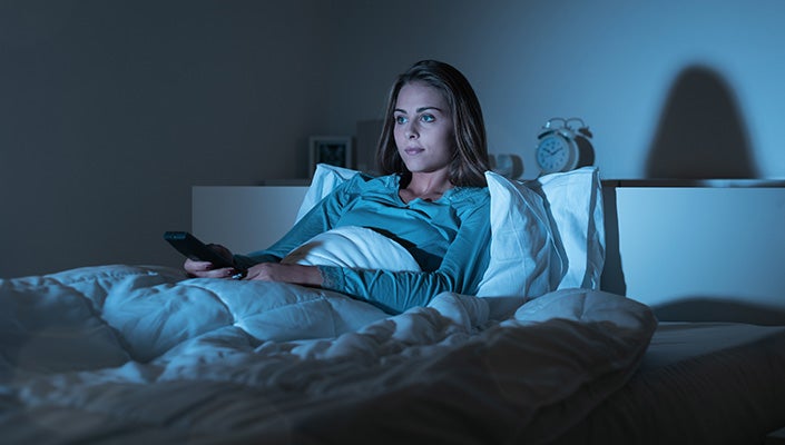 A woman sits up in bed, watching a screen