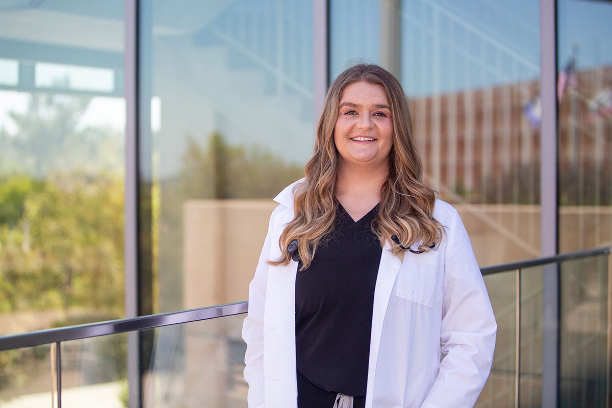 Cheyenne Matyac wearing scrubs and a white coat outside of a hospital