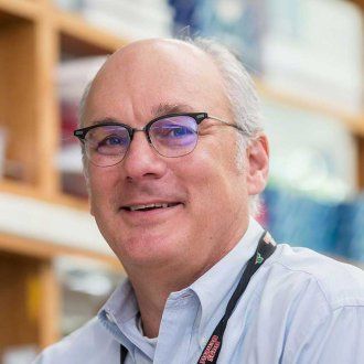 Man with glasses smiling with a lab out of focus in the background