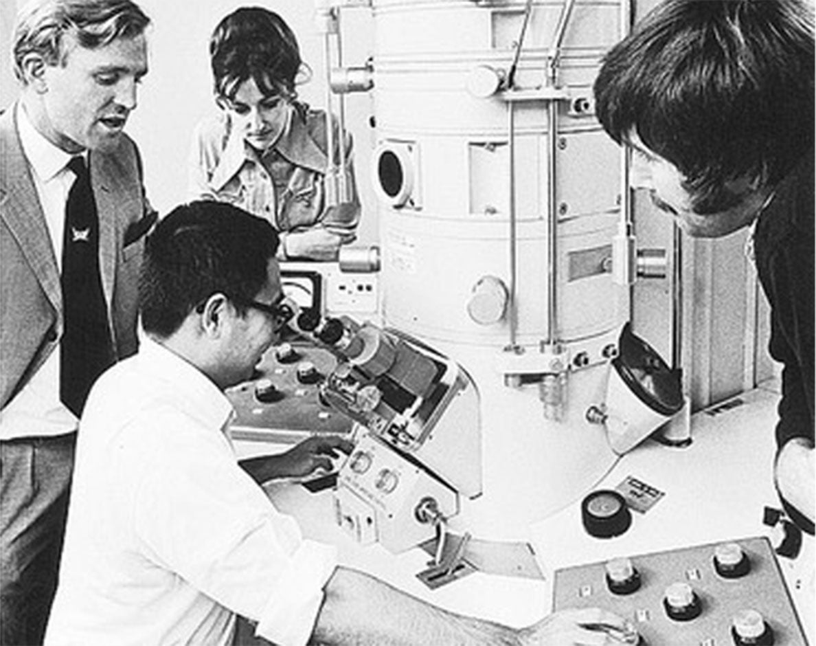 A black and white photo of four scientists looking at a large machine, date 1960