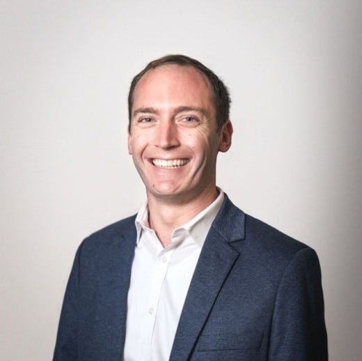 Man in suit jacket with no tie smiles at camera