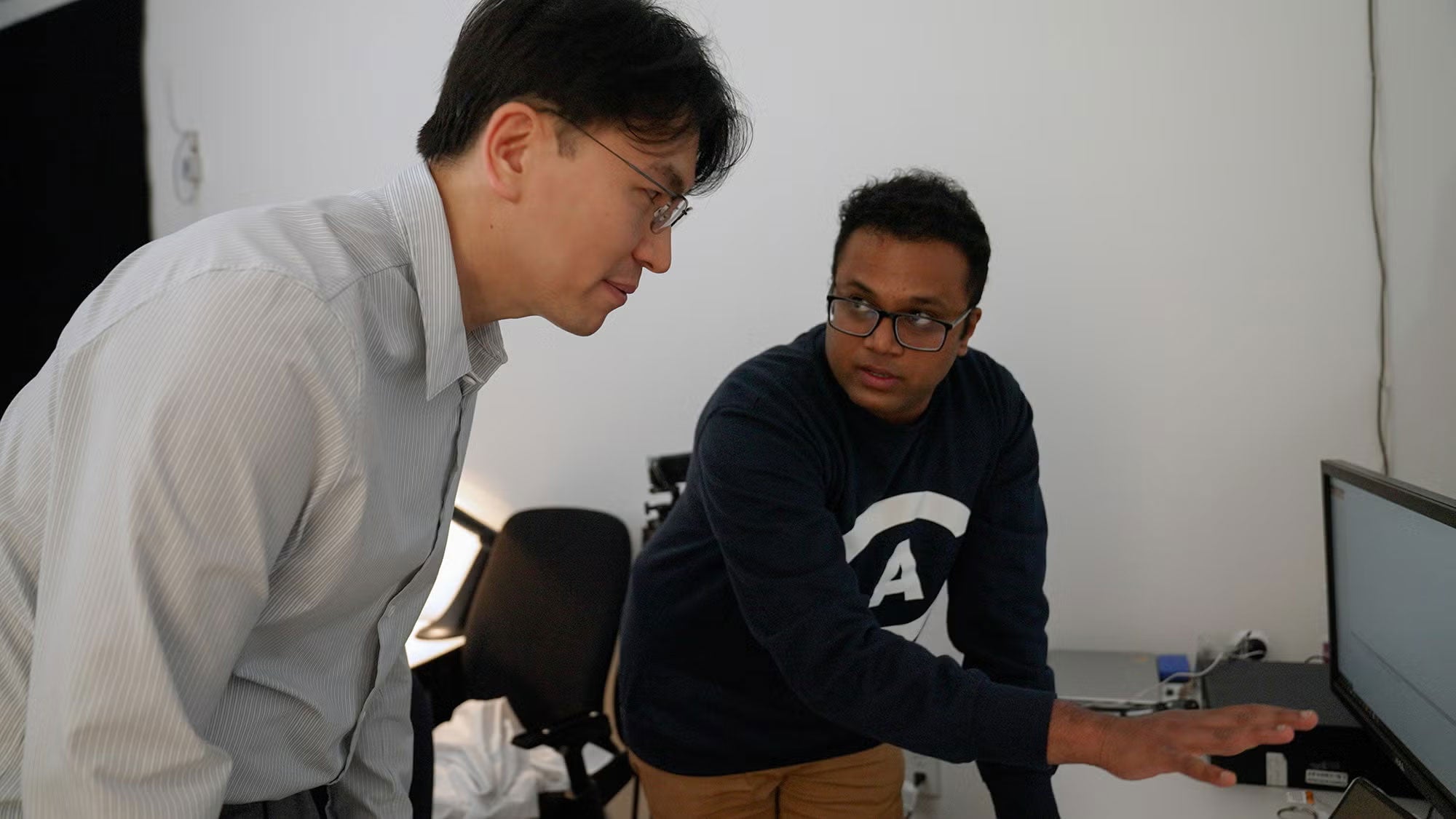 Two researchers look and gesture at a computer screen.
