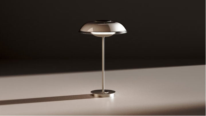 A silver, modern lamp casts a shadow on a light table top.