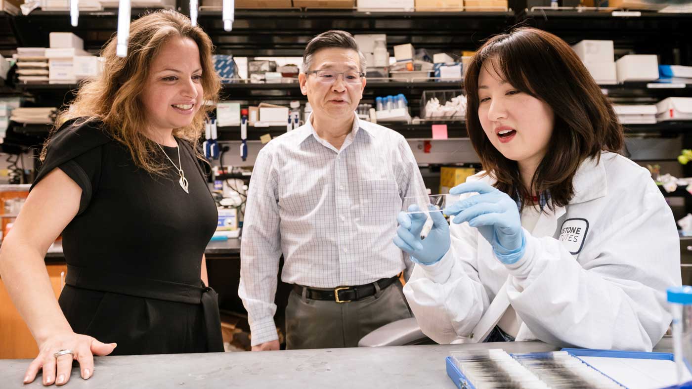 Three people look at a slide someone is holding in a lab
