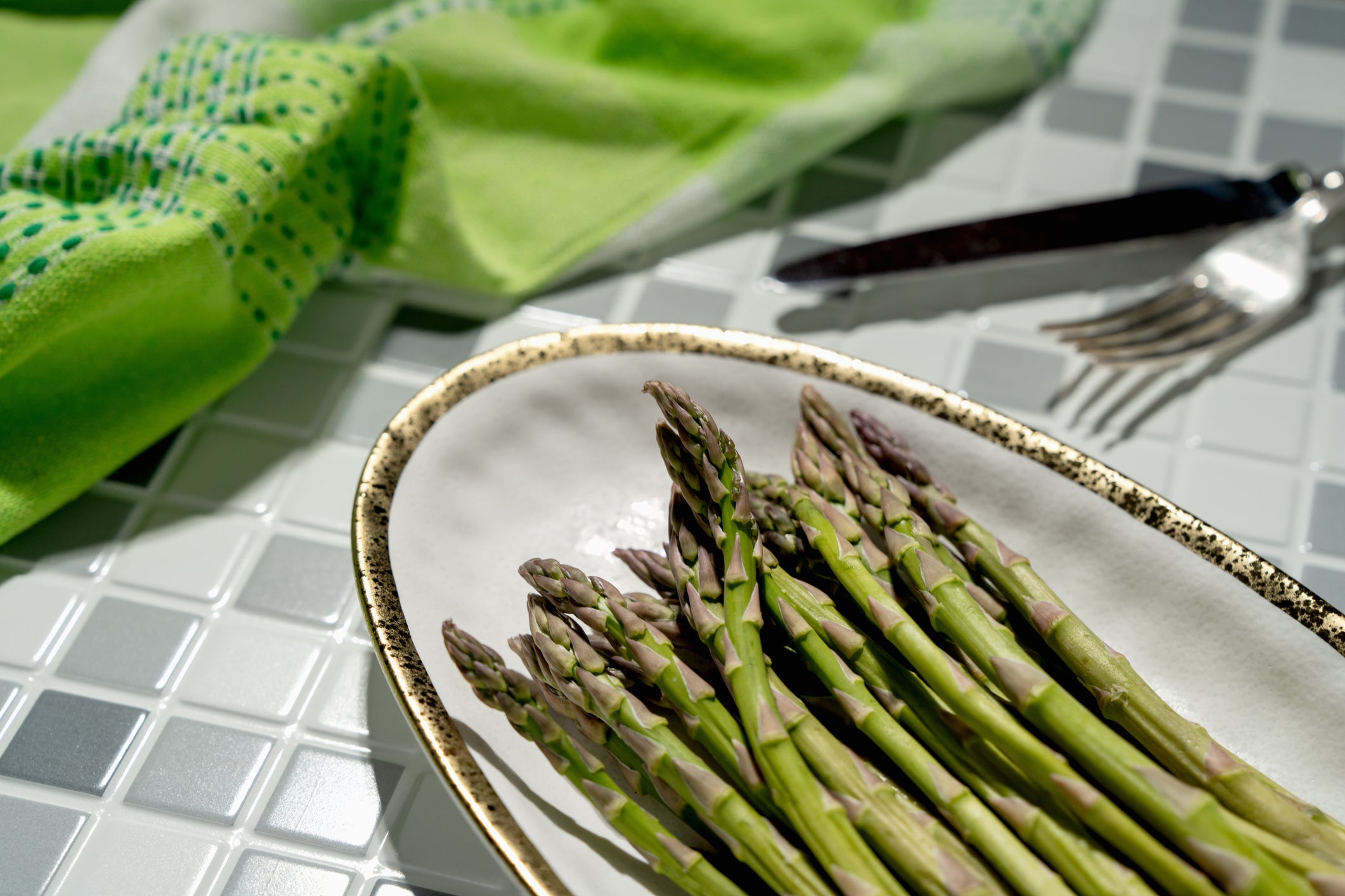 Asparagus on a platter on a table with a fork and knife