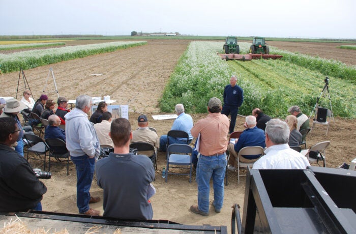 A group of people listen to someone talk on a farm