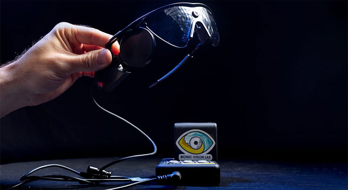 A hand holds up a pair of glasses with a camera attached to it