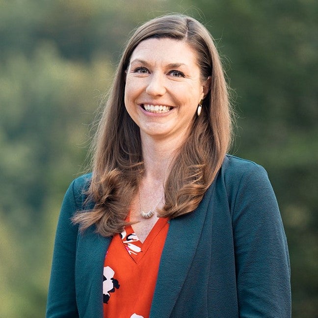 Heather Hochrein smiles at the camera wearing a teal blazer and red blouse