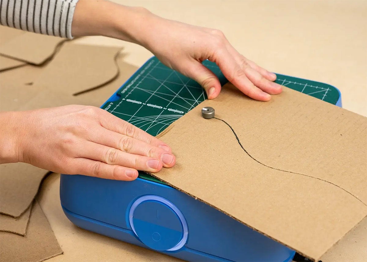 A woman's hands guide a piece of cardboard through a kids-specific table saw.