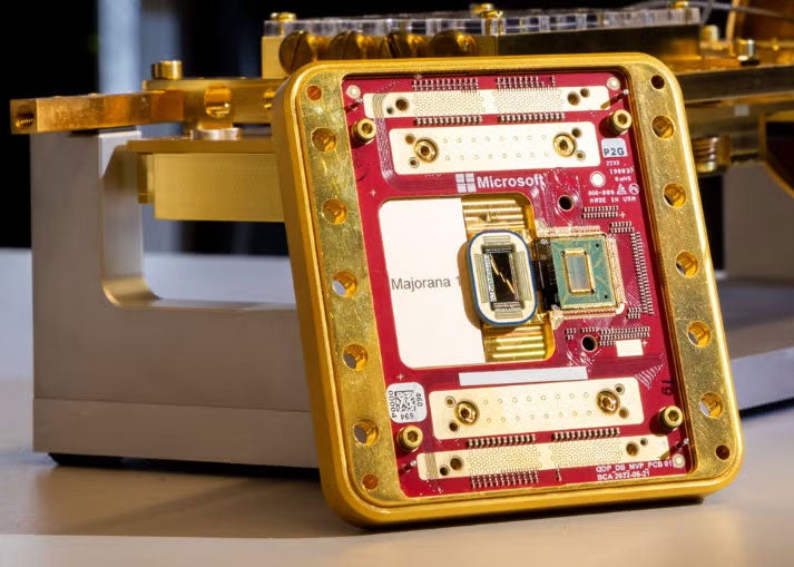 A large gold an red computer chip, labeled Majorana 1, rests against a shiny bit of equipment on a table top 
