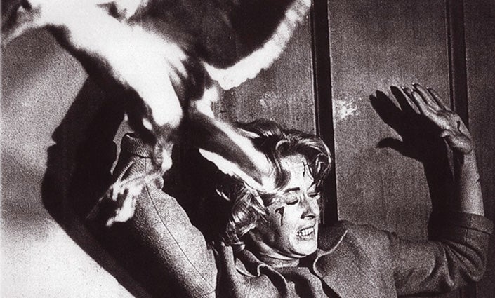 A woman acting in a horror films, arms up and disoriented after being attacked by a bird