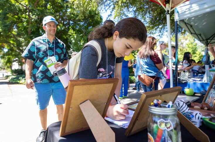 A father looks on as a pre-teen signs a paper at a table on the UC Riverside campus