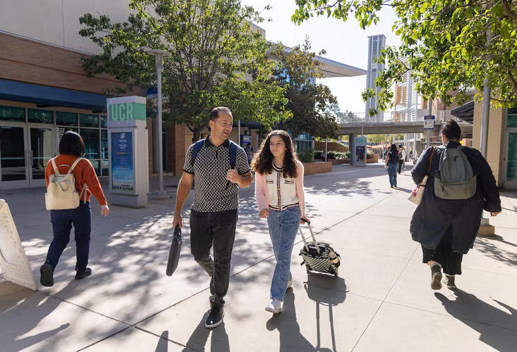 A man walks through the UC Riverside campus with his daughter pulling a bag alongside him as they talk