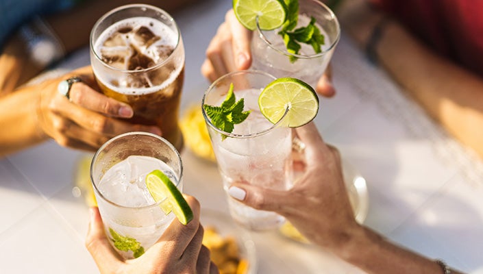 Four icy glasses with limes on their rims are clinked together at a bar