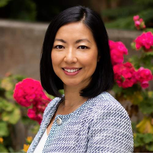 Doris Wang smiles at the camera in a headshot photo in front of big magenta flowers