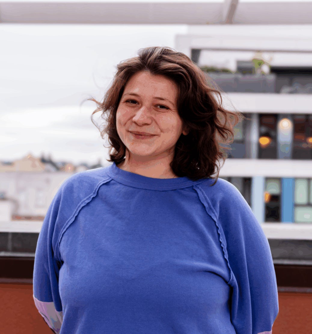A woman in a blue shirt smiles on a rooftop outdoors