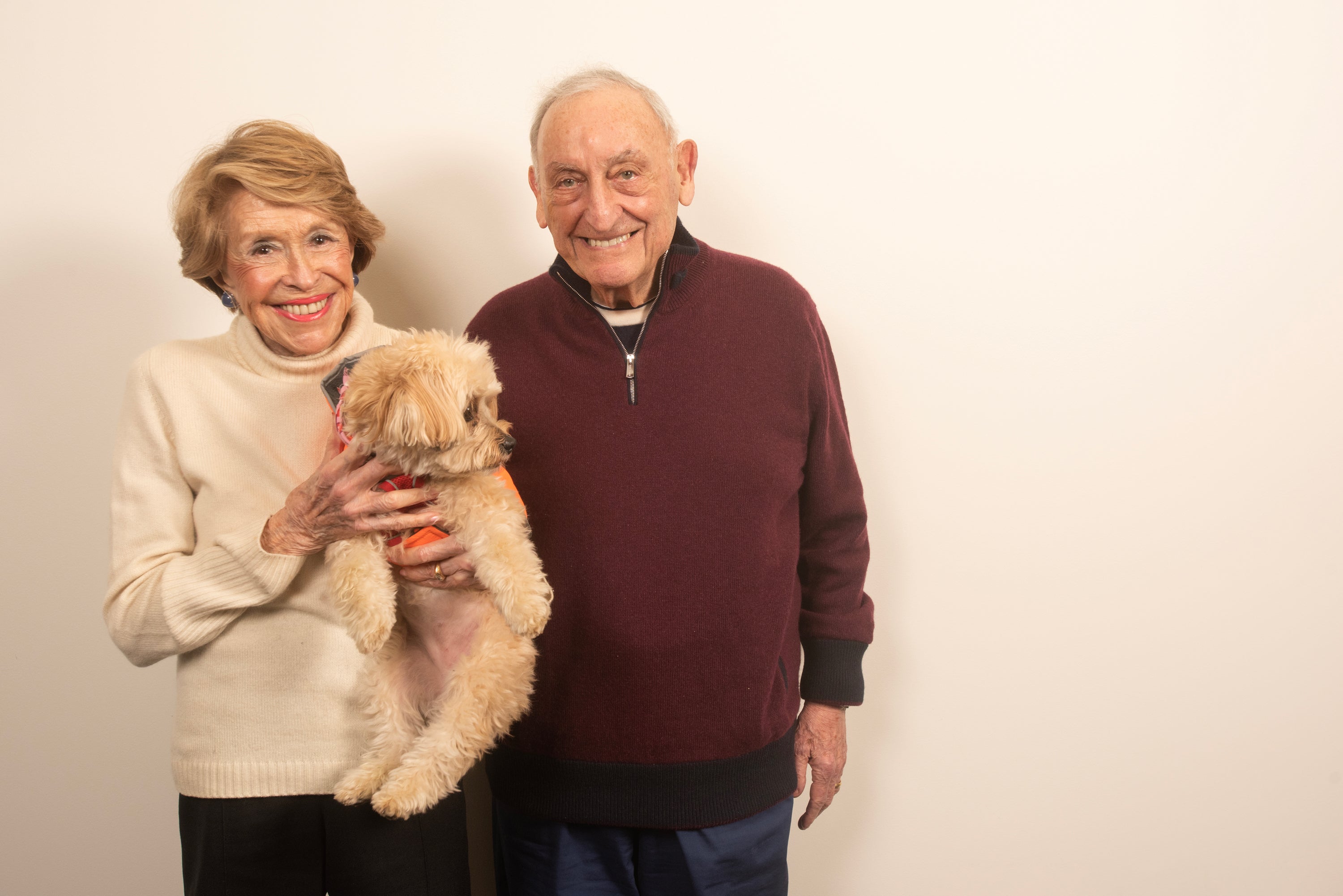 A woman holds a dog while a man stands next to her, both smiling