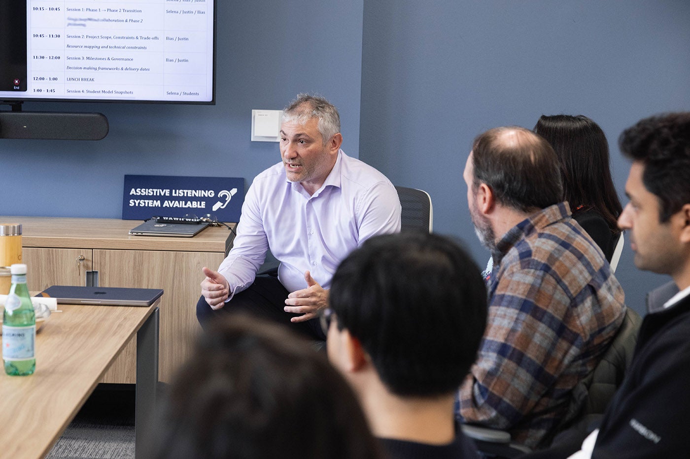 A man at a conference table speaks to a group of people
