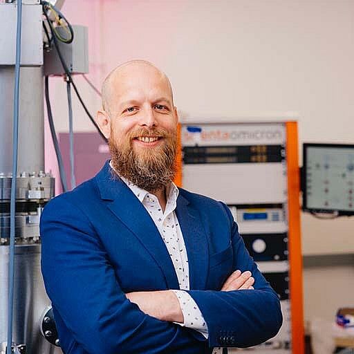 A man in a blue blazer with a long beard in a lab
