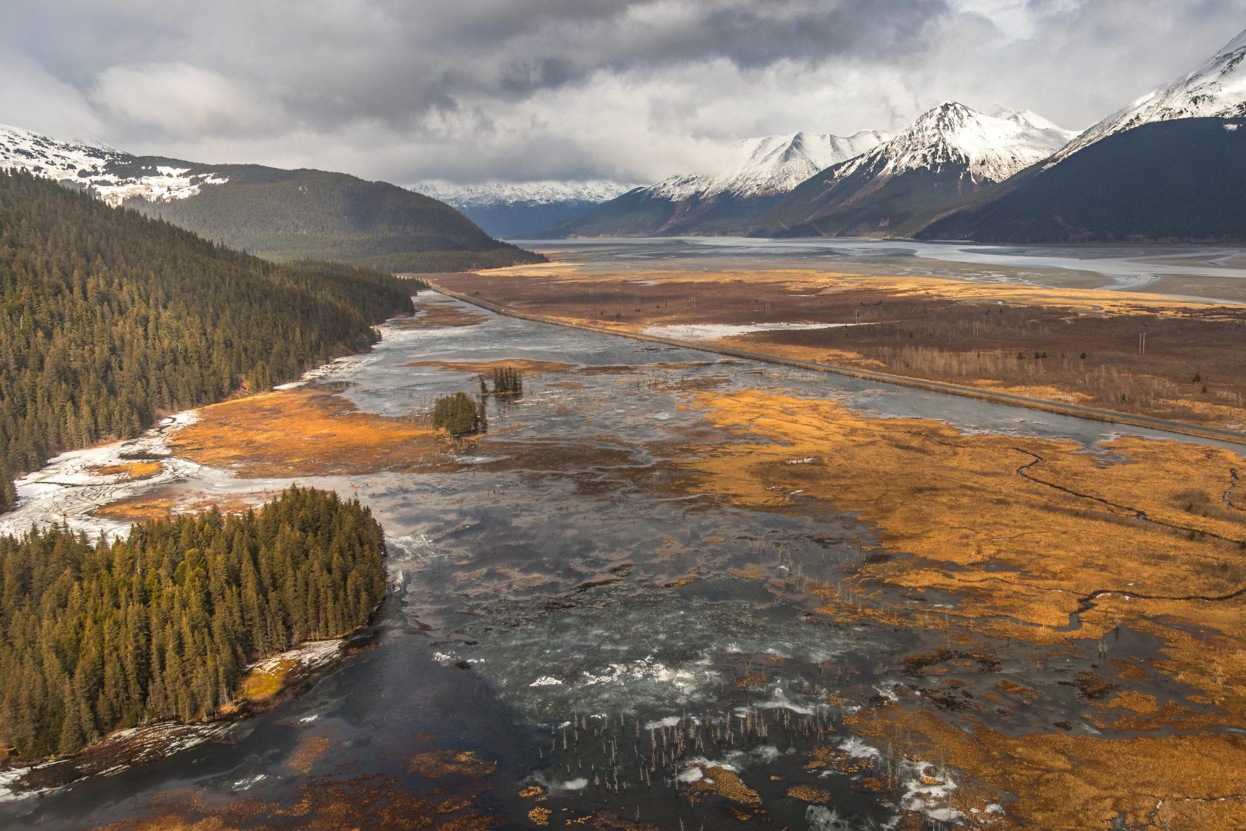 A body of water in a wilderness area seen from overhead, with snow-capped mountains in the background