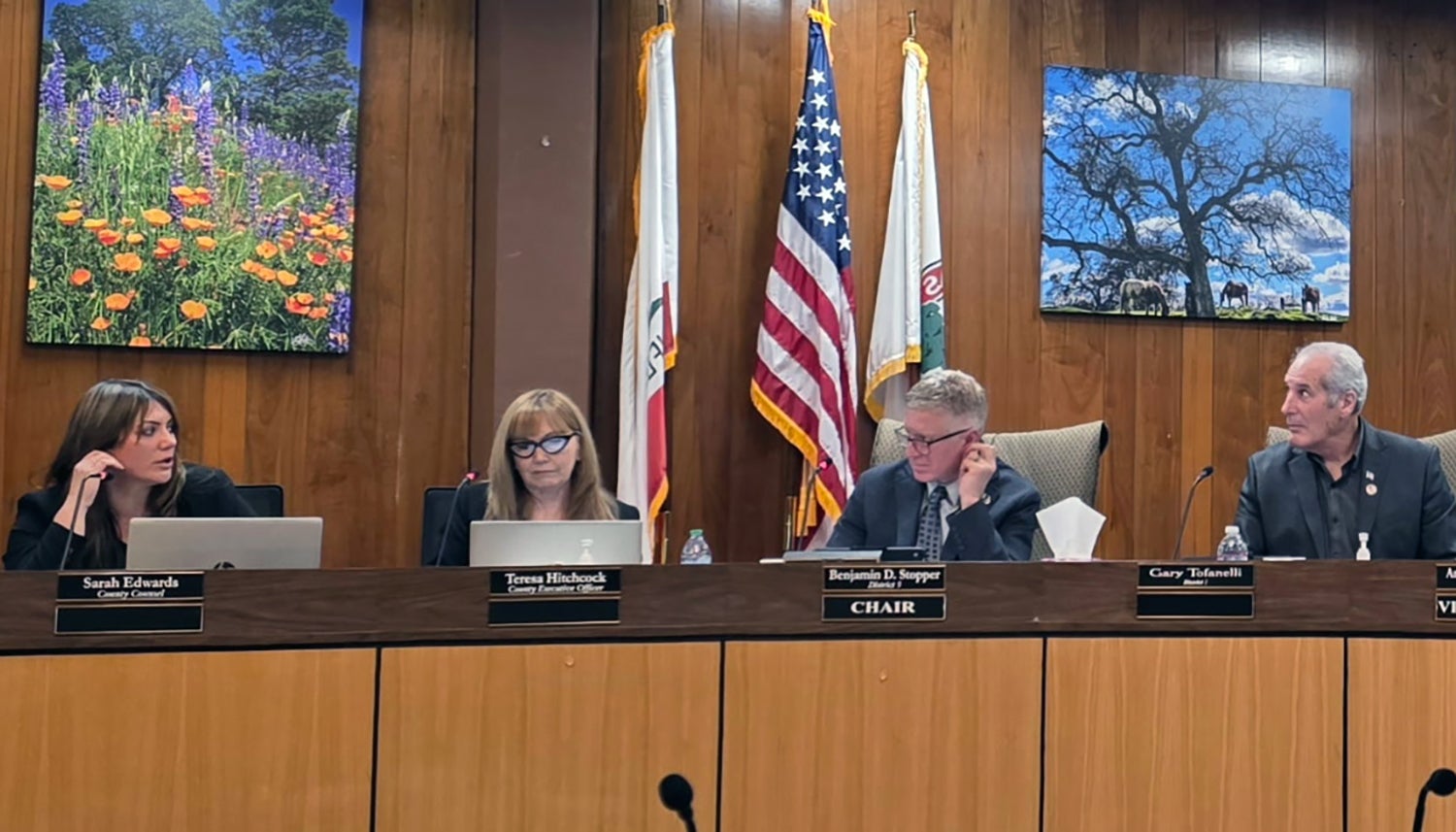 On the left two women seated at an official meeting, on the right, three men, 