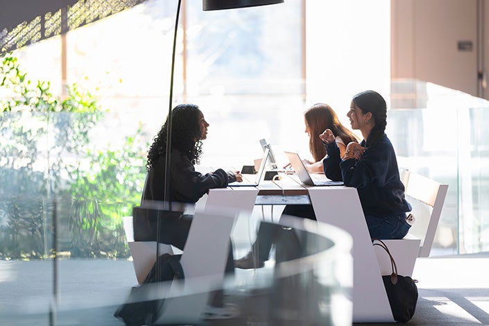 Three students talk across a table in a common area shielding them from sun