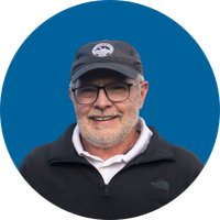 A man with a baseball cap, glasses and a white beard smiles in a headshot