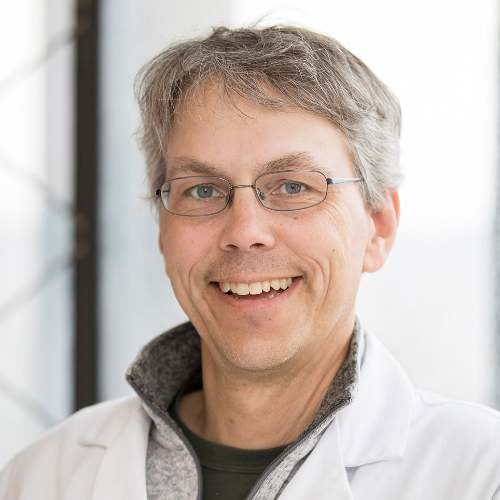 A man with glasses in a lab coat smiles