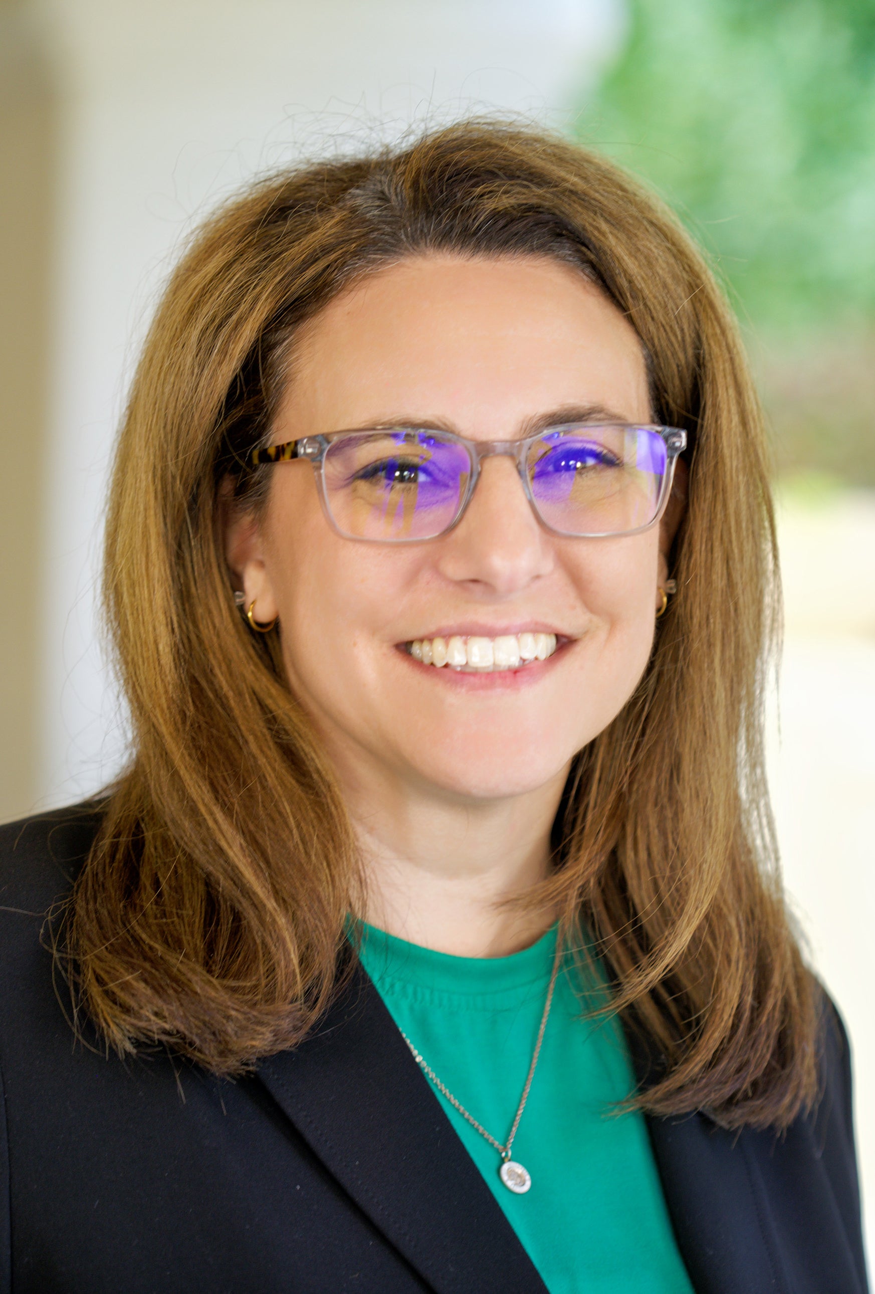 Woman in glasses and green top and dark blazer smiles in portrait