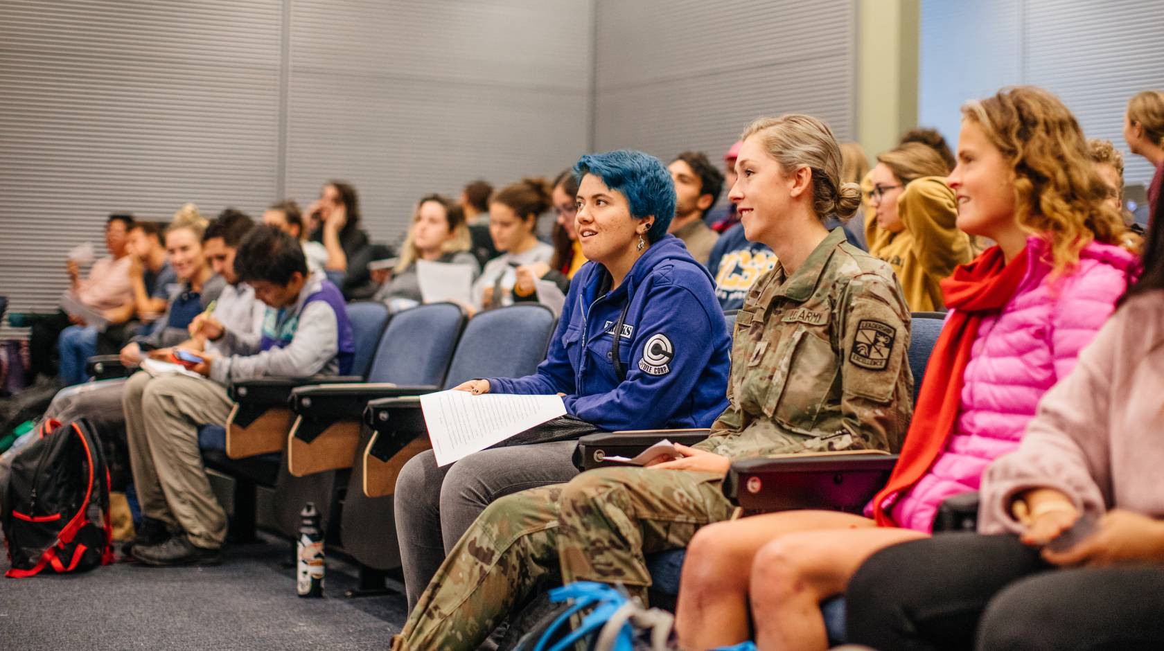 A woman in a U.S. Army uniform sitting in a lecture hall full of students
