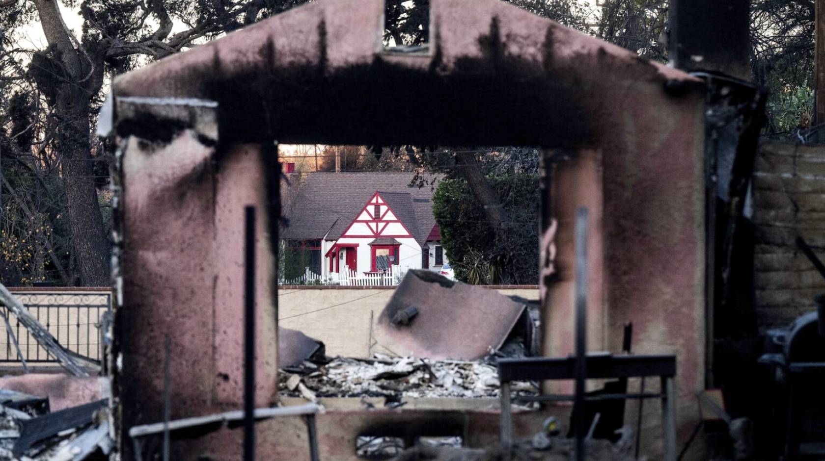 A home destroyed by the Eaton Fire stands in front of a home that survived in Altadena.