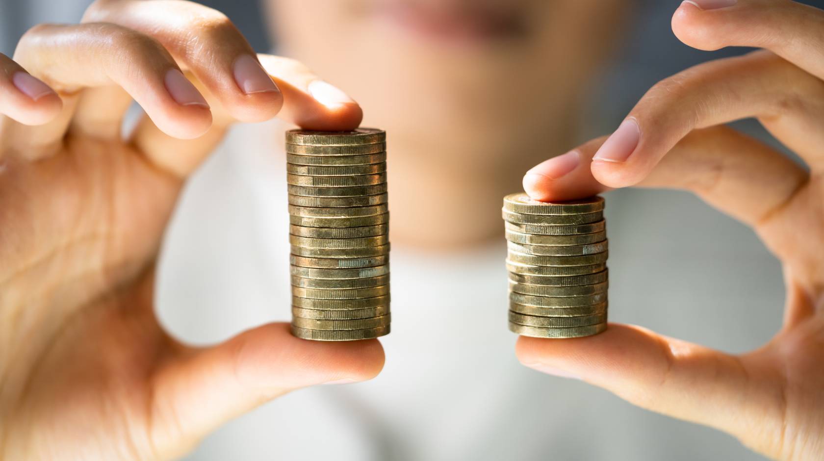 Close up of hands holding two stacks of coins, one larger than the otther