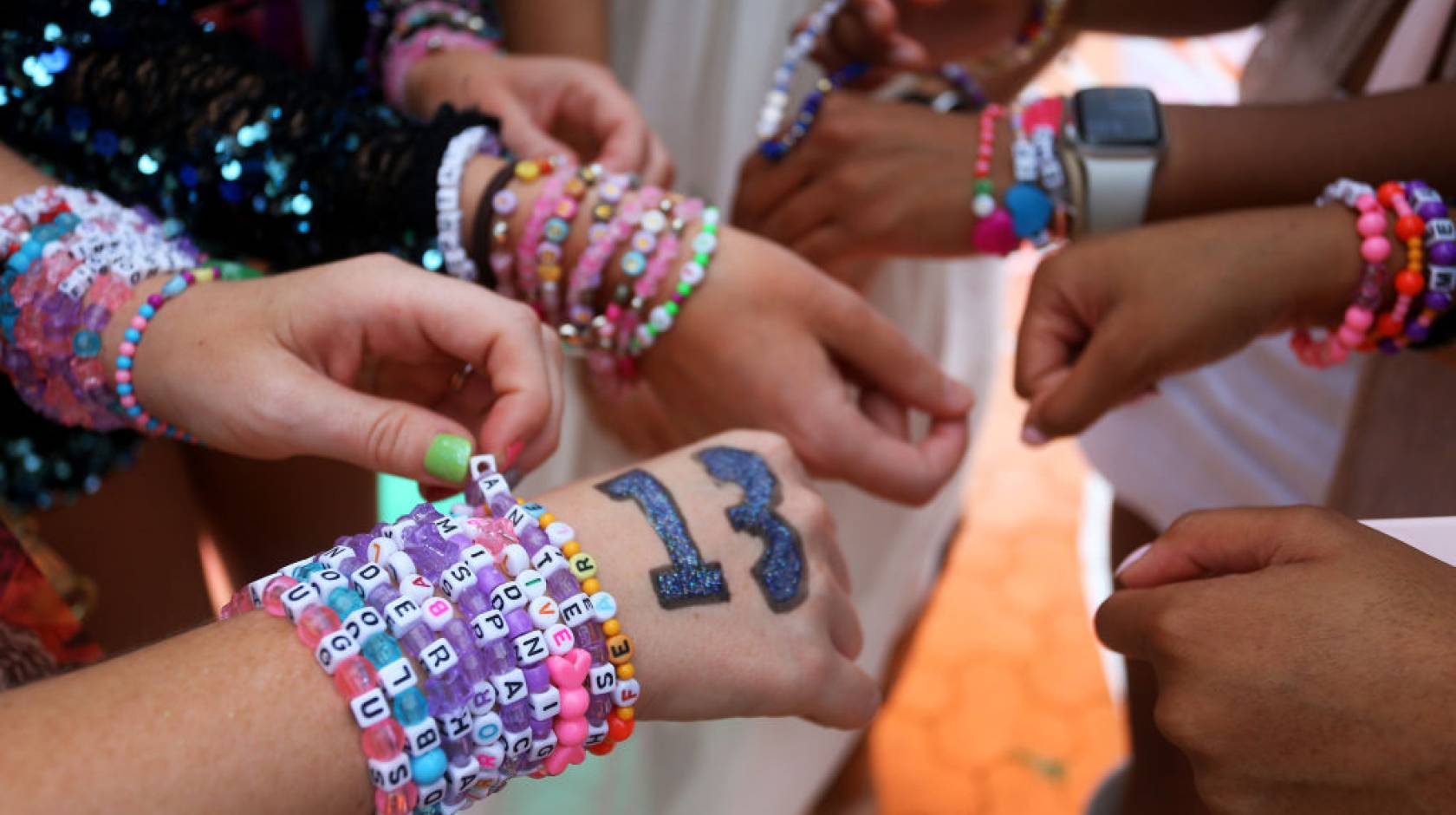 Closeup of the hands of a group of Taylor Swift fans wearing stacks of colorful friendship bracelets