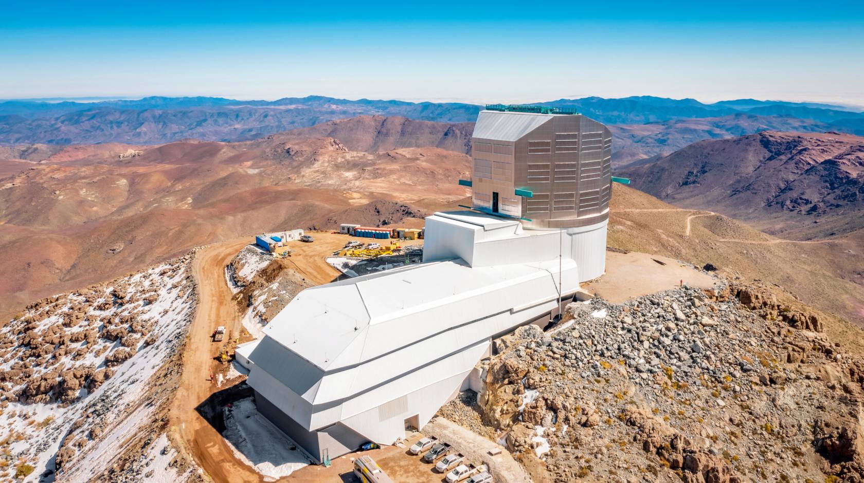 A huge, modern building atop a remote, snow-covered mountain, with desolate mountains stretching into the distance