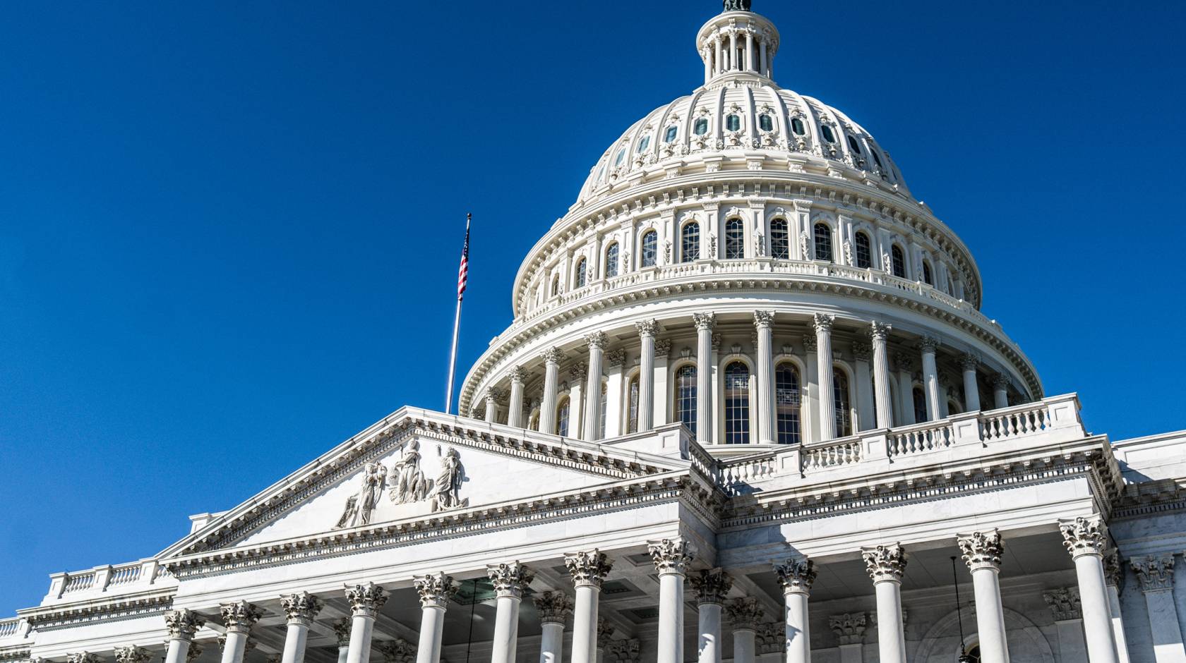 The U.S. Capitol building viewed from an angle against a bright blue sky