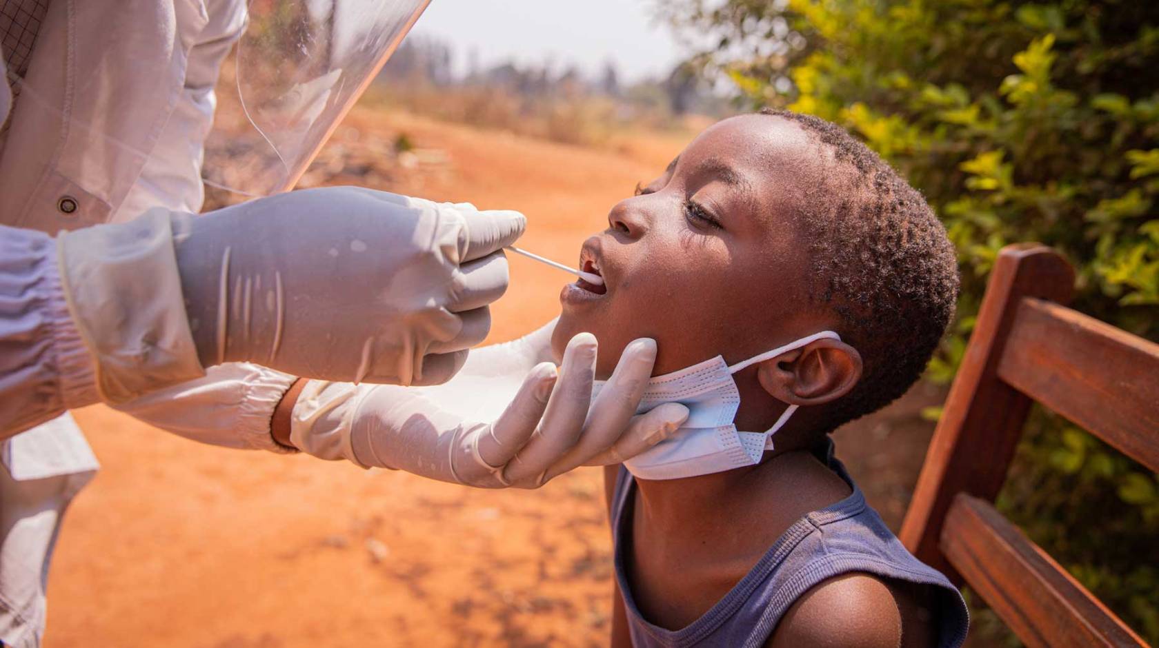 A young African child gets a tongue swab test from a medical professional.