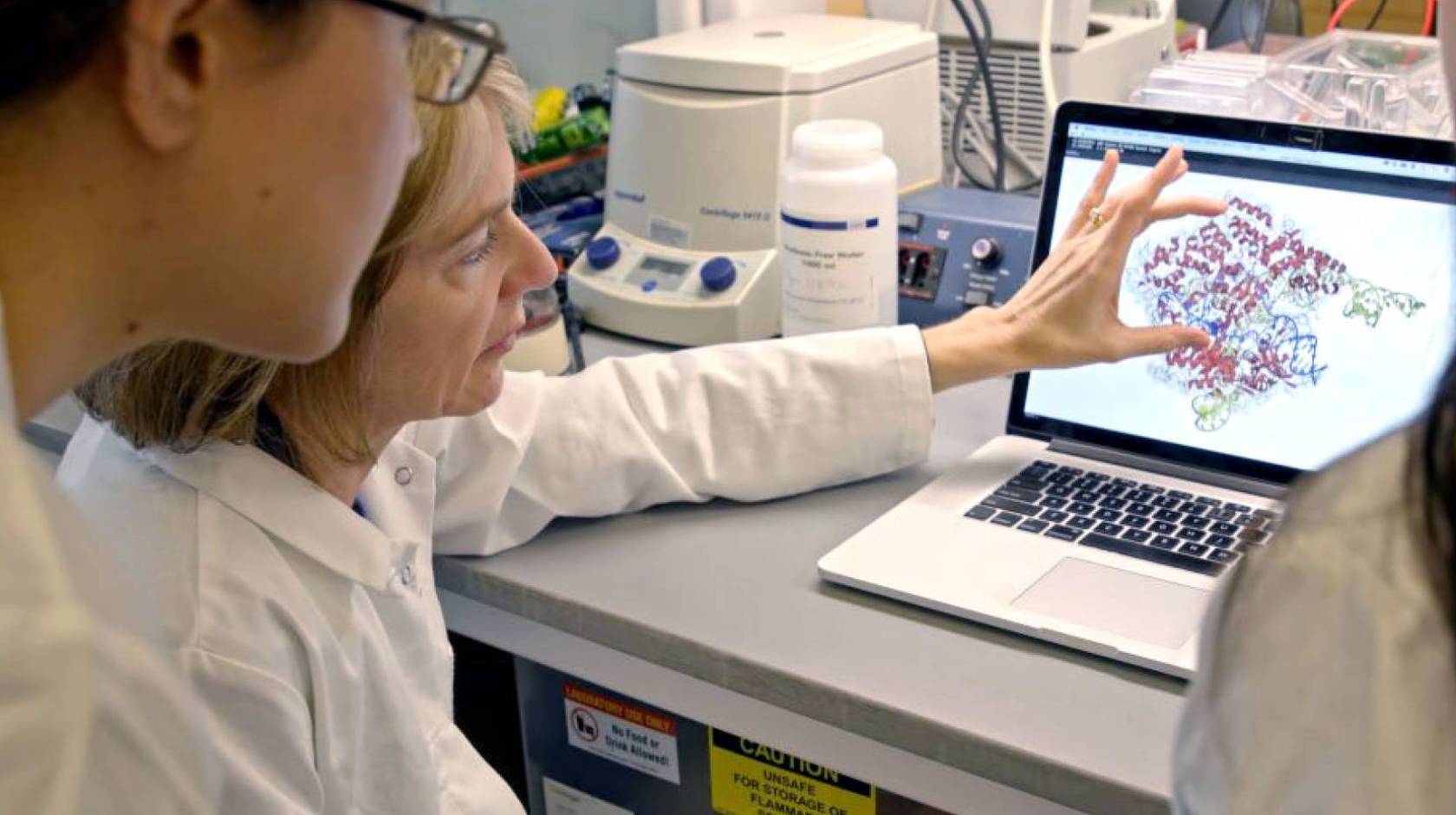 A woman doctor in a lab coat shows a male student a molecule on a computer