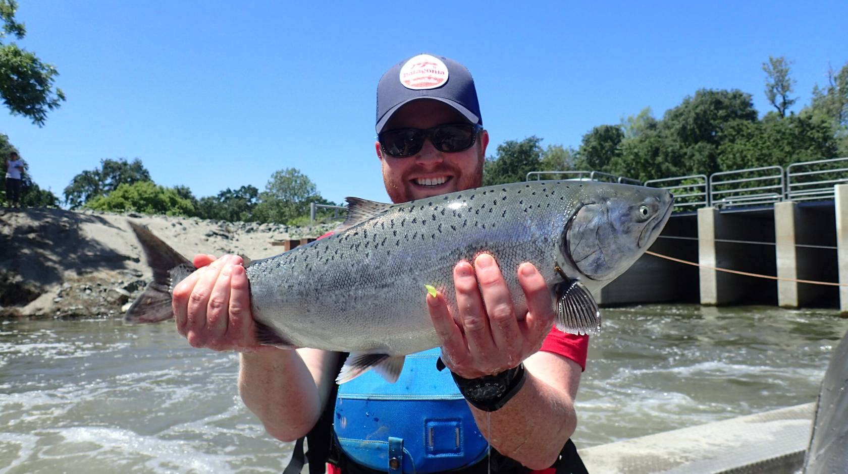 A man holds up a salmon in front of a rushing river
