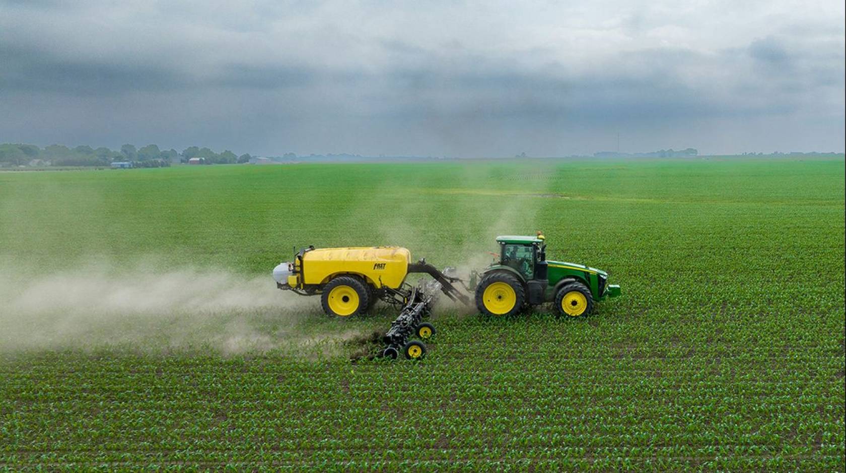 A tractor sprays pesticides on a green field under a gray sky