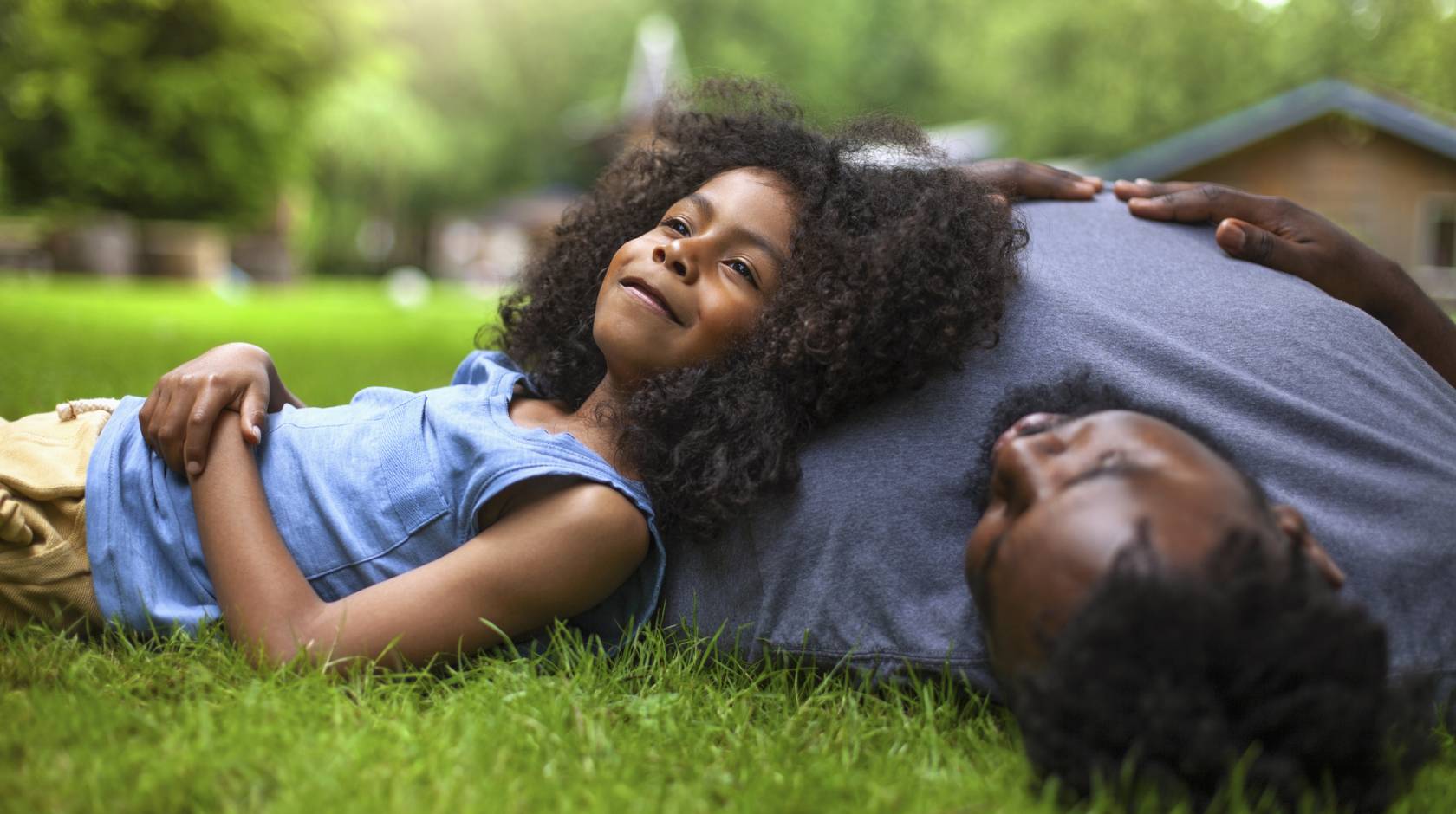 A young girl reclines against her father's shoulder on fresh grass